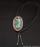 Full view of vintage Navajo turquoise and coral bolo tie on black background.