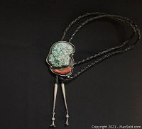 Full view of bolo tie showing braided leather cords, silver tips, and pendant with blue green turquoise and red coral stones