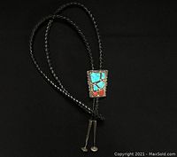 Full view of the bolo tie showing braided cords and silver centerpiece with turquoise and coral insets.