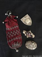 Four jewelry items on black background: mesh chatelaine with marcasite and chain, silver Wellesley College pin, floral garnet and pearl brooch, oval filigree silver pin
