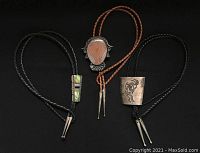 Three vintage sterling silver bolo ties on braided leather cords displayed on black background showing distinctive designs and signed metal slides.