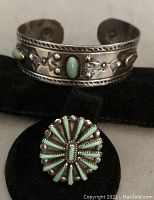 Image showing silver cuff bracelet with two green turquoise oval cabochons, stamped rope edges and floral designs, one turquoise stone missing.
