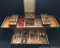 Opened gold leatherette jewelry box showing multiple compartments filled with assorted costume jewelry including necklaces, earrings and pins.