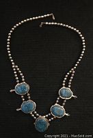 Full view of necklace laid flat on black background showing double strand silver beads and five turquoise stone settings.