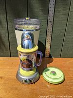 Frozen drink maker assembled with base, pitcher, and separate lid on wooden surface with ruler background.