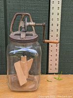Full view of the vintage glass jar butter churn with wooden paddles inside and metal hand crank with wooden handle, ruler for scale.
