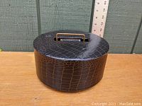 Circular black faux alligator leather covered poker chip carousel on a wooden surface against a wall with measurement ruler behind it for size reference.