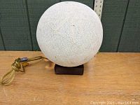 Spherical wound string lamp shade on a wooden base with power cord and switch.