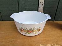 White ceramic 5 quart Dutch oven with orange floral and fruit decoration, side view and handle visible against ruler for scale.