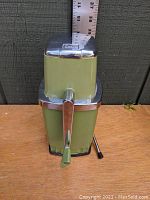 Front view of avocado green mid-century Sears ice crusher showing crank handle and overall body shape.