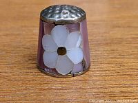 Front view of the vintage thimble showing the mother of pearl flower inlay on a pinkish background with a metal top.