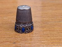 Front view of the vintage metal thimble with lapis lazuli insets on the base, showing detailed metalwork and stone setting.