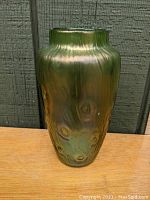Front view of green iridescent art glass vase showing textured circular rusticana pattern and swirling surface.