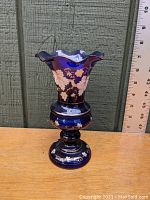 Full side view of cobalt blue blown glass vase with white enamel foliate decoration and flared ruffled rim