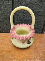 Front and side view of vintage Fenton peach blow basket showing ruffled peach-pink rim, maple leaf decorations, and original Fenton label on the body.