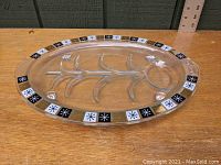 Clear glass well platter with embossed tree pattern and atomic starburst design around edge, shown on wooden surface with ruler for scale.