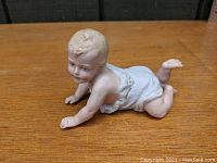 Photo showing side view of porcelain baby figurine crawling with one leg bent upward, detailed hand and foot sculpting visible
