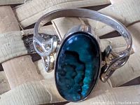 Front view of the sterling silver ring with large oval abalone stone, showing vibrant blue and green colors with swirling patterns and polished silver setting.