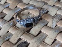 Sterling silver ring with black onyx rectangular stone placed on woven surface showing front and side details