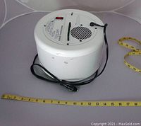 Side and underside view of the AEROX air purifier showing cylindrical perforated white metal housing, attached black power cord, and measuring tape for scale.