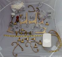 Photo of the entire lot spread out in a container showing various brass hooks, hinges, doorknobs, and other fittings with a tape measure for scale.