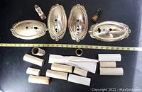Four brass oval wall sconce backplates and multiple white ceramic socket covers laid out with measuring tape for scale.