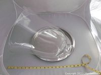 Large clear glass dome cloche resting on a round metal tray with measuring tape beside showing size.
