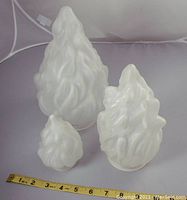 Three frosted flame shaped glass lighting shades grouped together on a flat surface, with measuring tape showing sizes and rounded base fittings visible.