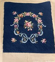 Close-up view of cross stitch wreath with floral design and blue ribbon on navy fabric