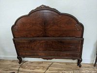 Front view of the burled walnut headboard showing carved floral details and curved top.