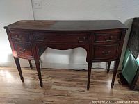 Front view of the mahogany buffet server showing its curved front, three drawers, and tapered legs on a hardwood floor