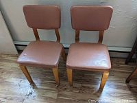 Front view of two brown vinyl and wooden frame mid-century side chairs, showing upholstery and seat condition.