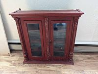 Full view of the antique red painted cupboard with glass front doors, carved columns, and lock.