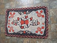 Full view of the rectangular hooked rug with a floral design and braided border on a tile floor.