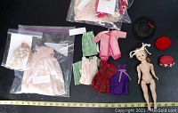 Photo showing nude vintage Madame Alexander doll with disconnected head and multiple handmade doll clothes and hats arranged around it, some in clear plastic bags.