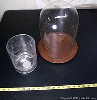 Top-down photo showing both the glass dome on its wooden base and the small clear vase side by side on a black surface with ruler indicating size.