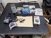 Overview of all items including Canon PowerShot S40 camera with box, Vivitar 2600 flash, Canon Sure Shot AF35M film camera with case, and other accessories spread on black table.