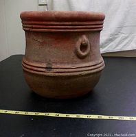 Side view of the terra cotta planter showing horizontal ridges and loop decoration around the body with measuring tape for scale.