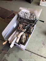 Tub containing assorted household electronics and items such as rotisserie, cords, paper, and vinyl strips.