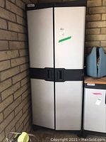 Front view of Stanley plastic tool cabinet against brick wall, showing two grey doors with black handles.