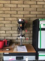 Front view of the Craftsman Laser Trac drill press on workbench with manual and measuring tape nearby.