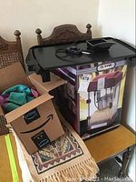 Photo showing a boxed Classic Series Elite popcorn maker with a black griddle and controls resting on top, also visible cardboard box with cloths inside.