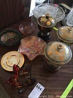 Wide view showing three hand-painted Shogan Kutani lidded porcelain pieces on wooden bases along with multiple decorative glass bowls and plates on a wooden table surface.