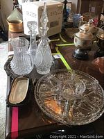 Two cut crystal decanters, large round glass relish tray with removable sections, and other glassware on wooden table.