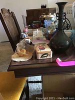 Side view of dining table with various small decorative items on top and one cane back chair with yellow seat partially visible.