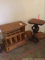 Wide view showing both the wooden magazine rack with drawer and the carved three-layer plant stand side by side on carpet.