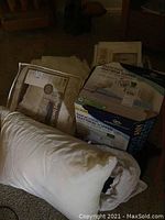 Photo showing quilted bedspreads, memory foam mattress topper boxes, and white pillow on floor.