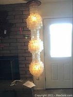 Photo showing entire 3-tier Capiz shell lamp hanging from ceiling, glowing softly with light inside.