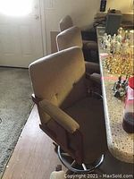 View of four upholstered bar stools lined up near a counter, showing the fabric upholstery, armrests, and wood base with metal footrest.
