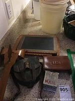 Compass in leather case, leather bullet case, handheld chalkboard, and metal mailbox bank shown on countertop